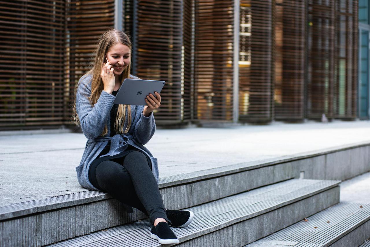 Smiling young woman working on a tablet outdoors in an urban setting.